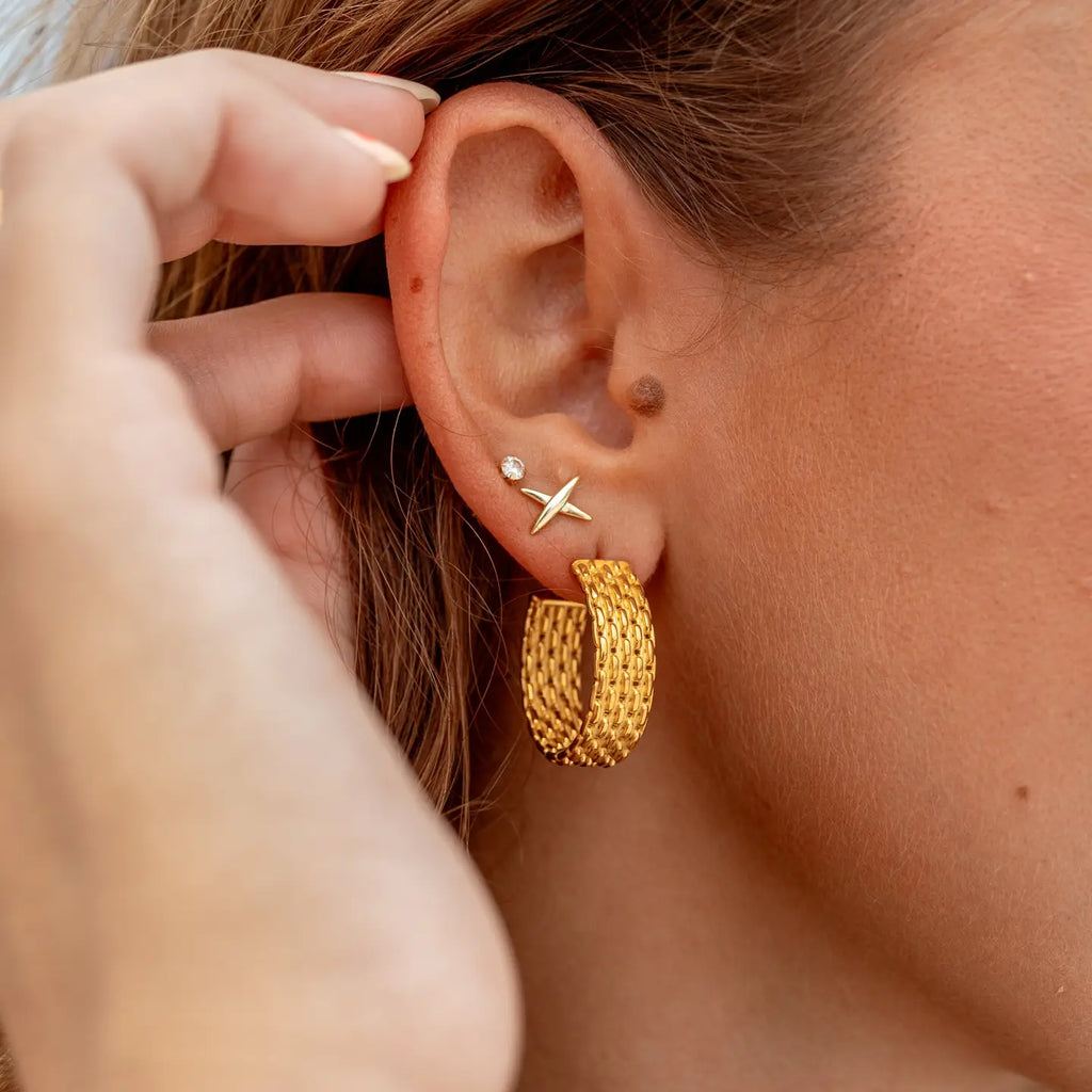Close-up of a person wearing gold hoop earrings with a starfish charm.