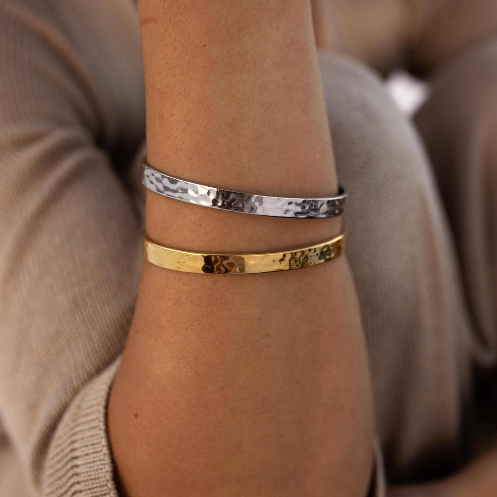 Close-up of a wrist wearing two bracelets, one gold and one silver, with a blurred background.