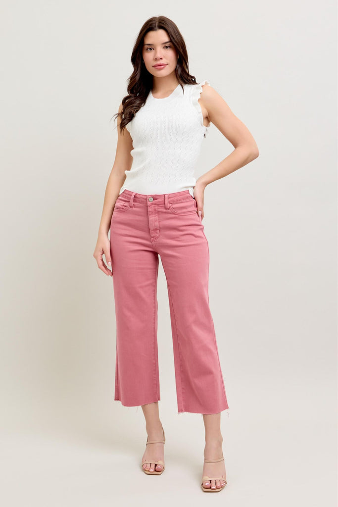 A person wearing Amelia Judy Blue high-waist wide leg crop jeans in rose color paired with a white sleeveless top. The cropped pants feature a raw hem and classic 5-pocket design, shown styled with neutral sandals against a light background.