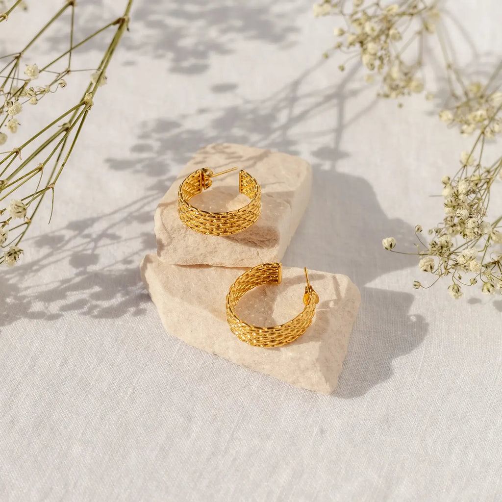 Gold hoop earrings on a textured stone surface with delicate flowers in the background