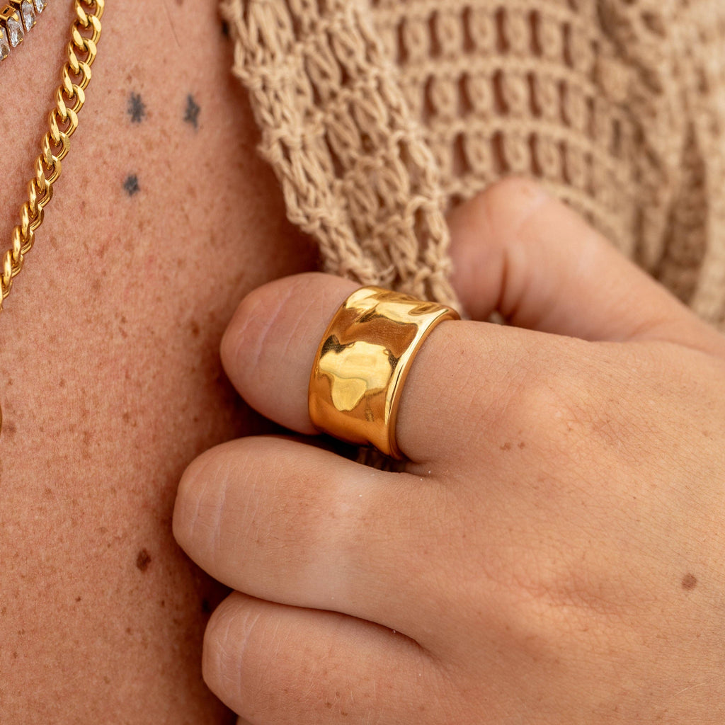 A person is wearing a gold-plated stainless steel ring with a geometric design on their finger.