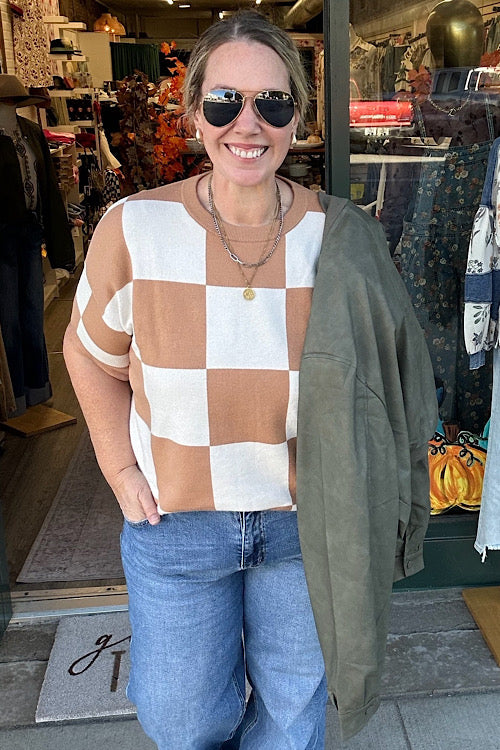 Woman wearing a checkered top and sunglasses holding green jacket in a store setting