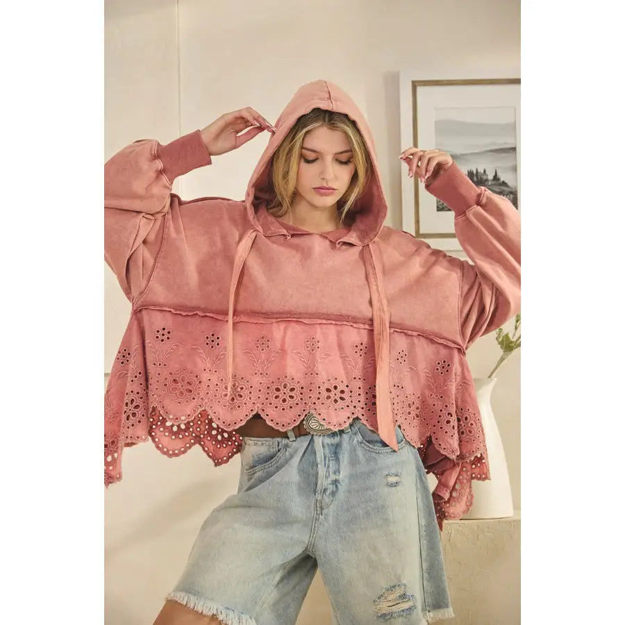 Person wearing a pink hoodie with lace details and light blue jeans indoors.
