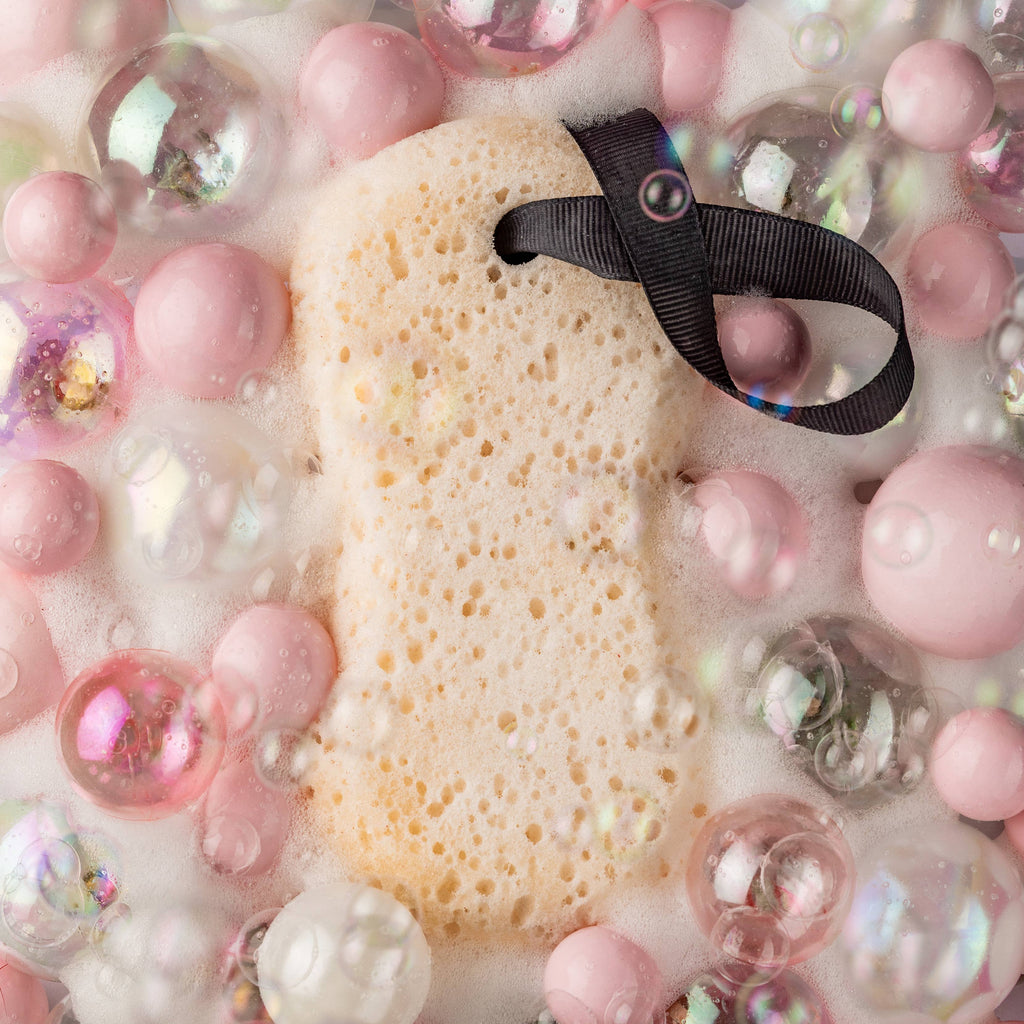 Sponge with a black hair tie surrounded by pink and clear spherical objects on a white background