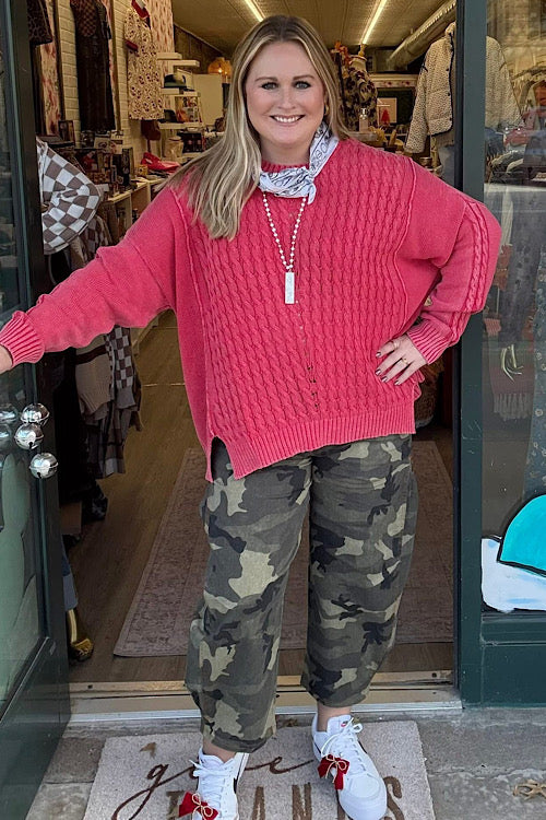 Woman wearing a pink sweater and camouflage pants standing in front of a store entrance.