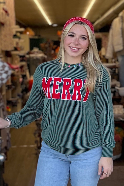 Woman wearing a green sweater with 'MERRY' in red letters, standing in a store.