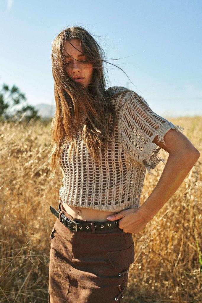 Woman wearing a crochet top and brown pants in a field with a clear blue sky.
