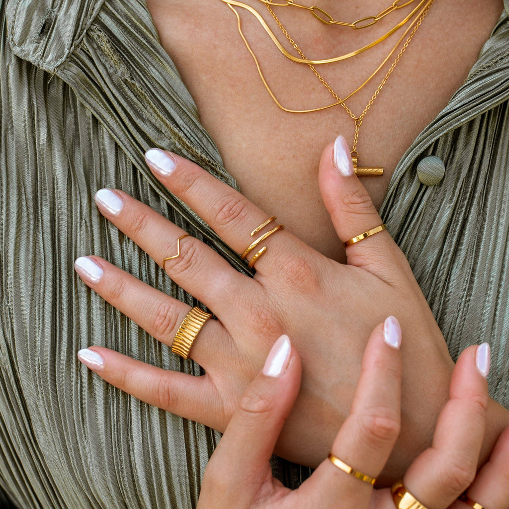 Close-up of hands wearing multiple gold rings with a neutral background