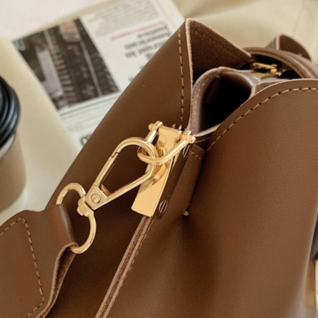 Brown leather handbag with gold clasp on a surface with a newspaper and coffee cup in the background