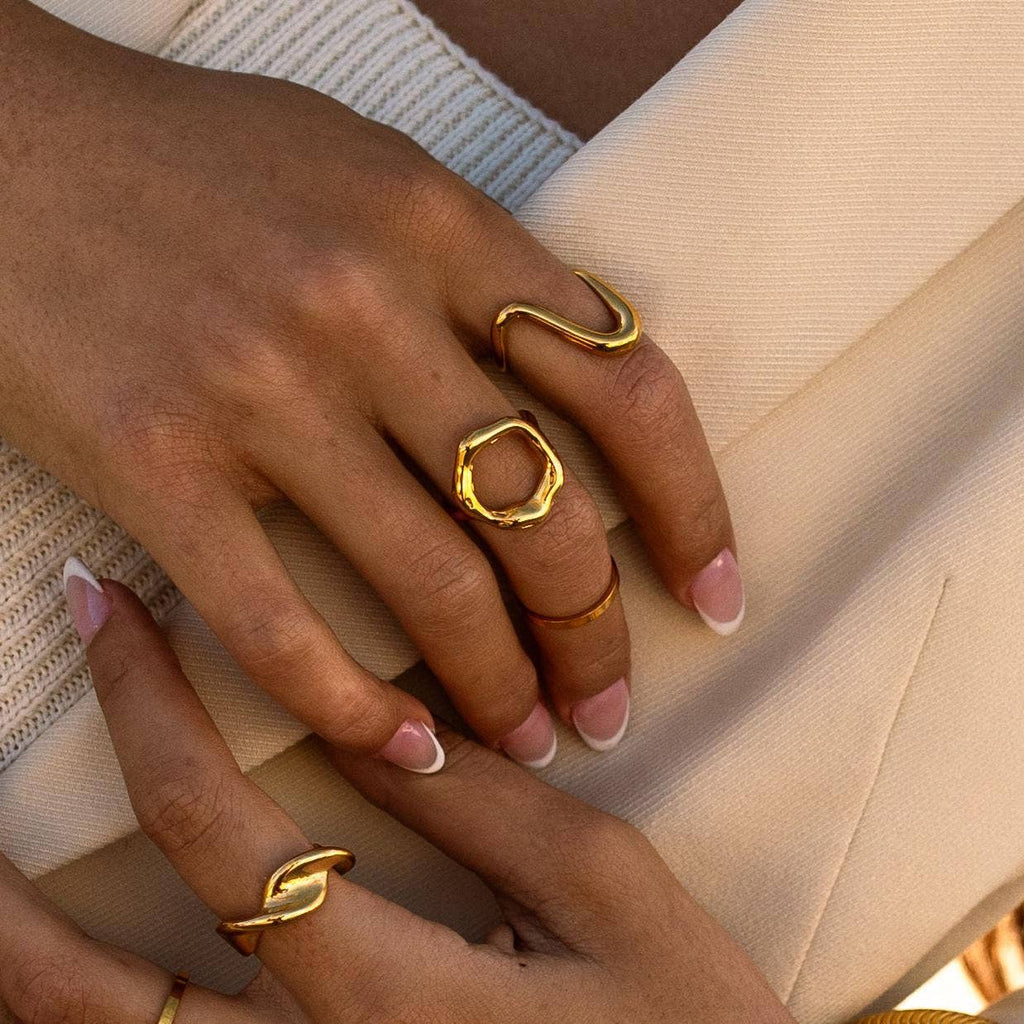 A gold-colored hammered metal ring on a person's finger, displaying an open circle design symbolizing new beginnings.

