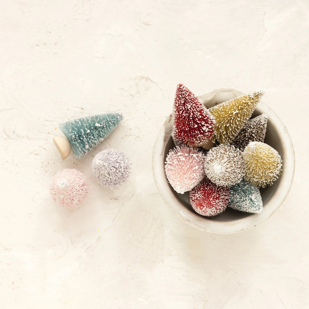 Set of 12 colorful sisal bottle brush trees with snow finish and wood bases, in assorted jewel tones for holiday decorating.