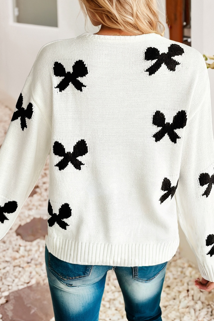 White sweater with black bow patterns worn by a person, standing on a carpeted floor.