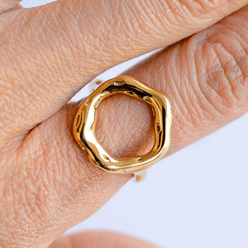 A gold-colored hammered metal ring on a person's finger, displaying an open circle design symbolizing new beginnings.

