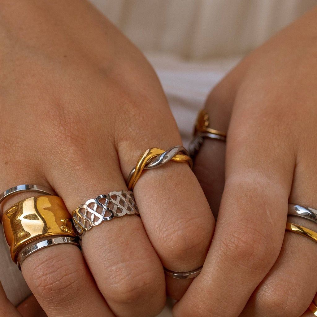 Close-up of hands wearing gold and silver rings on a neutral background