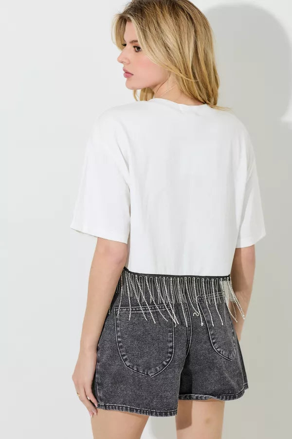 Woman wearing a white t-shirt and black denim shorts with fringe details on a plain background