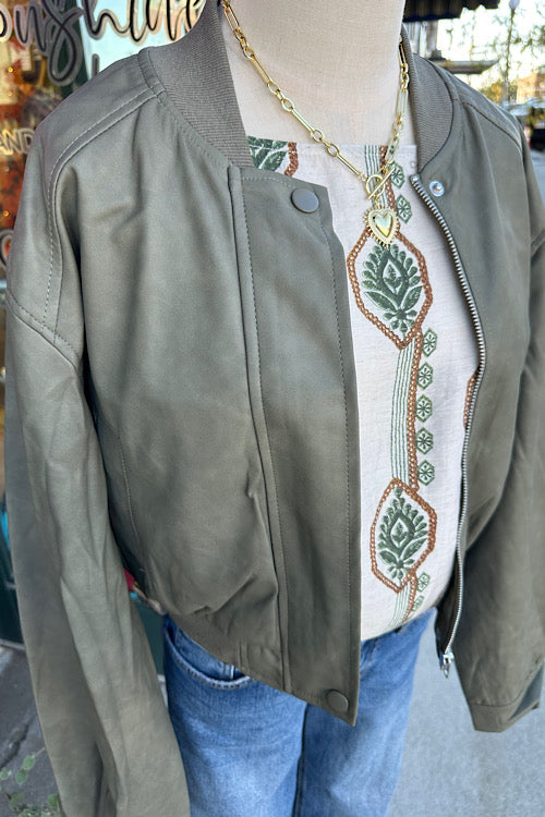 Mannequin wearing an olive green jacket over a white embroidered shirt with blue jeans.