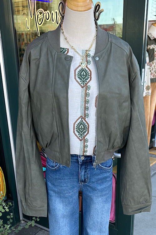 Mannequin wearing a green jacket, white embroidered shirt, and blue jeans in front of a store entrance.