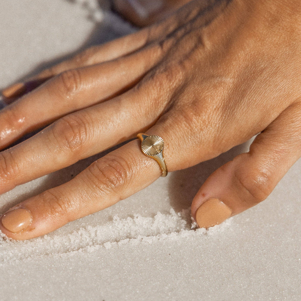 Hand wearing a gold ring on a sandy surface