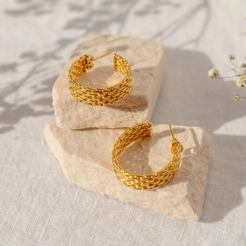 Gold hoop earrings on a textured stone surface with a soft background