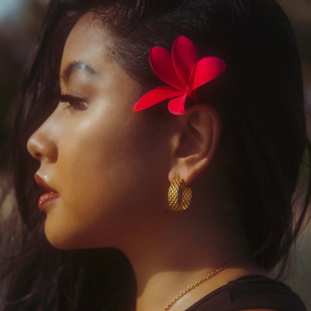 Woman with a red flower in her hair and gold earrings, looking away from the camera.