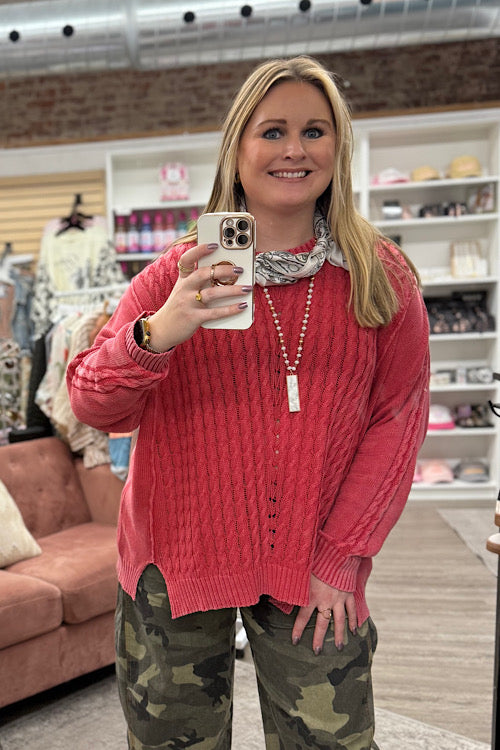 Woman taking a selfie in a store wearing a pink sweater and camouflage pants.