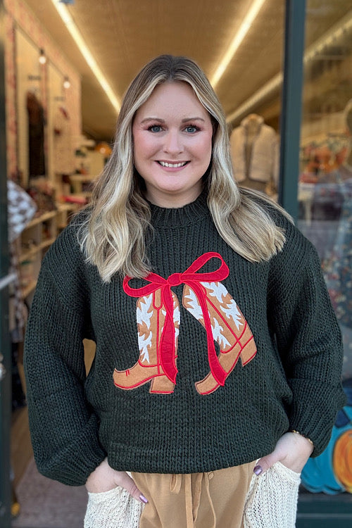 Woman wearing a green sweater with a red bow and boot design, standing in a store.
