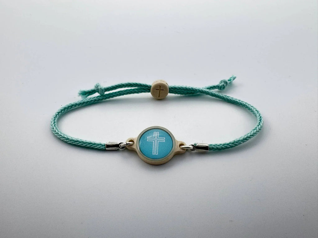 Turquoise bracelet with a gold clasp and cross charm on a light gray background