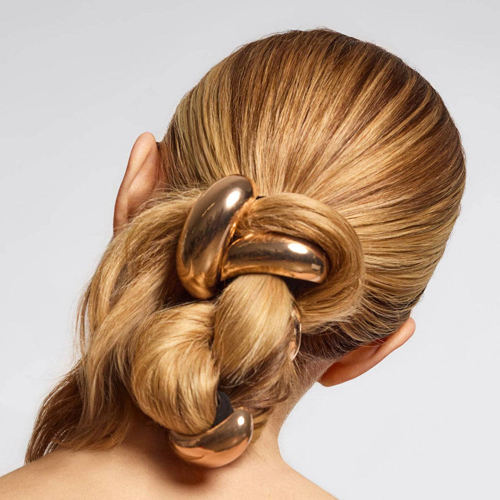Gold hair accessory in a styled bun on a neutral background