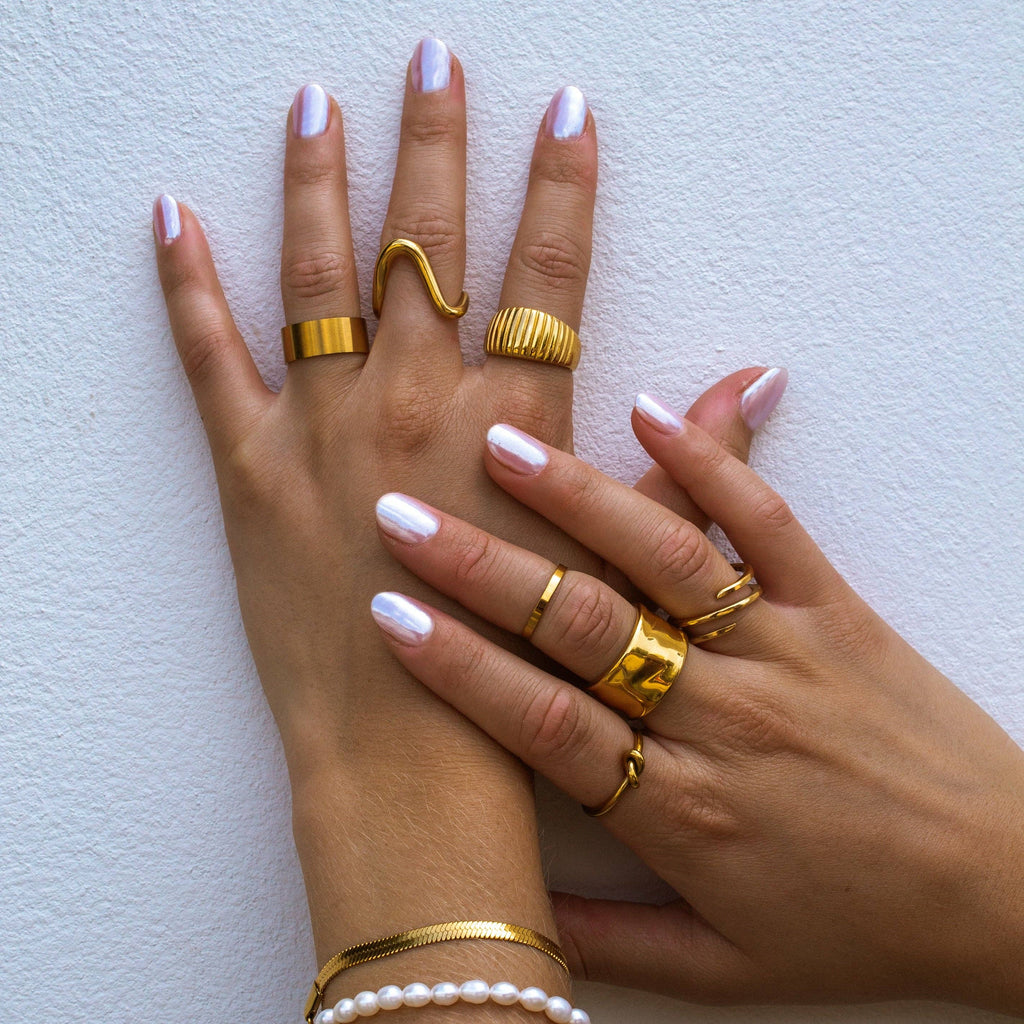 Hands wearing multiple gold rings on a light background