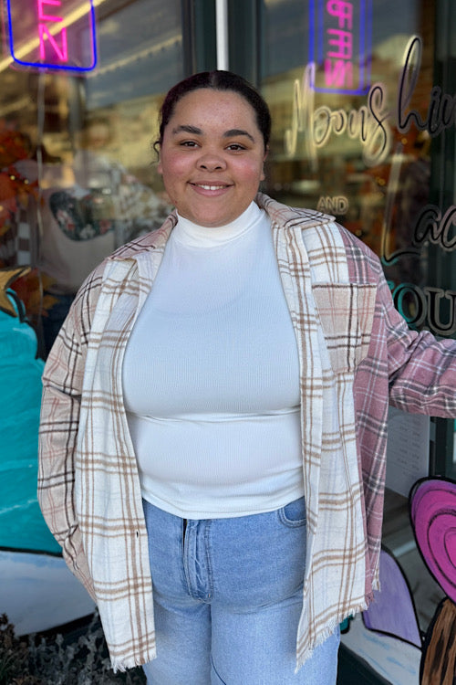 Person wearing a plaid shirt over a white top and jeans in front of a store window.