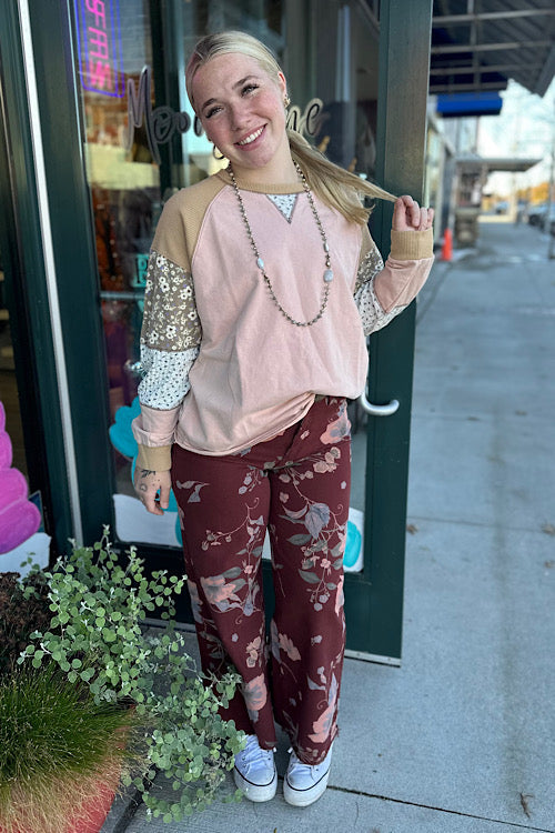 Woman in a pink top and floral pants standing outside a store.
