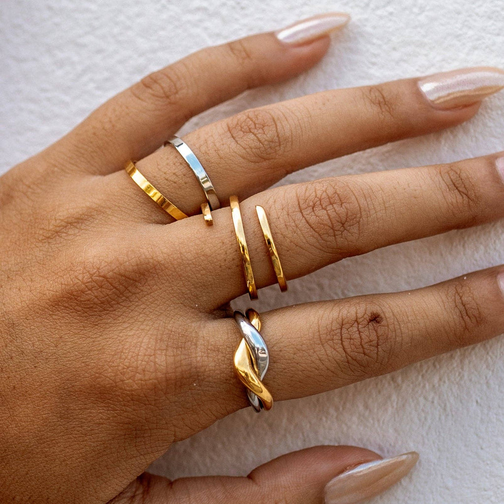 Hand wearing multiple gold and silver rings on a light background