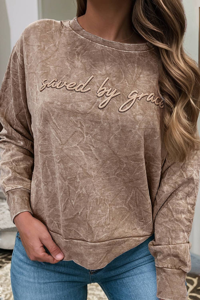 Brown sweatshirt with 'saved by grace' text worn by a person, indoors.
