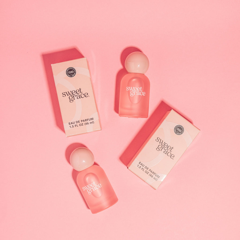 Two 'sweet grace' perfume bottles and their packaging on a pink background