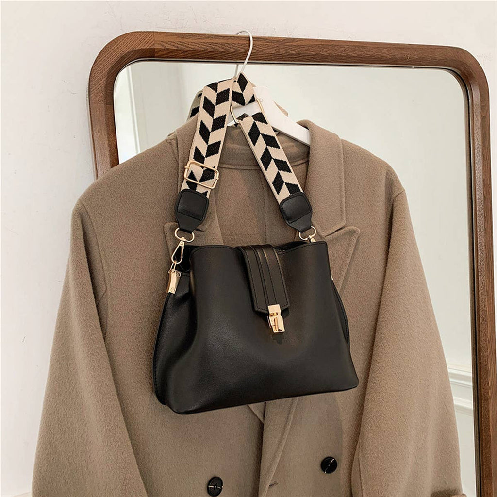 Black handbag with a patterned strap hanging on a coat in front of a mirror.
