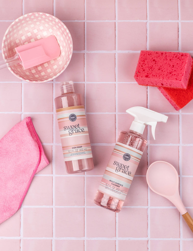 Pink cleaning products with accessories on a pink tiled background