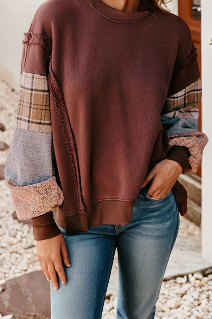 Person wearing a brown sweater with plaid sleeves and blue jeans outdoors.