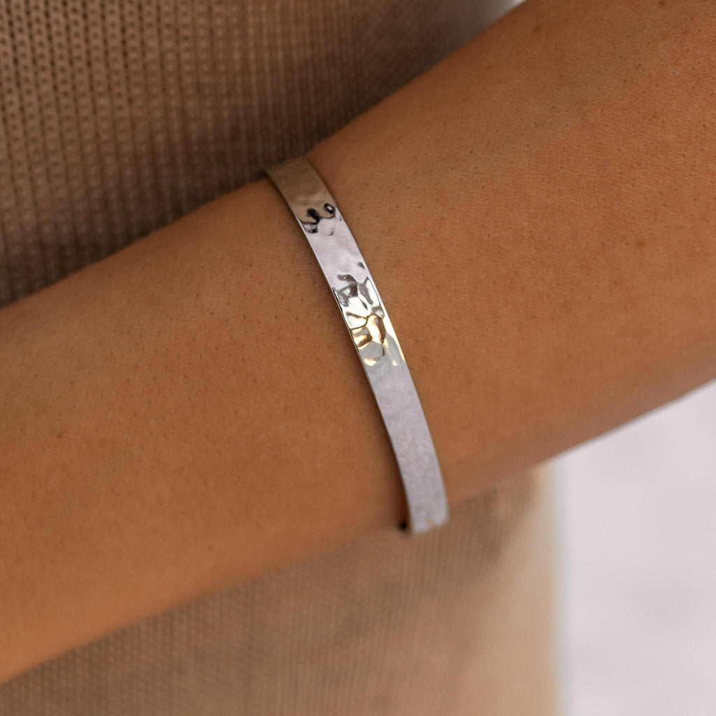 Silver bracelet with engraved design on a wrist against a neutral background