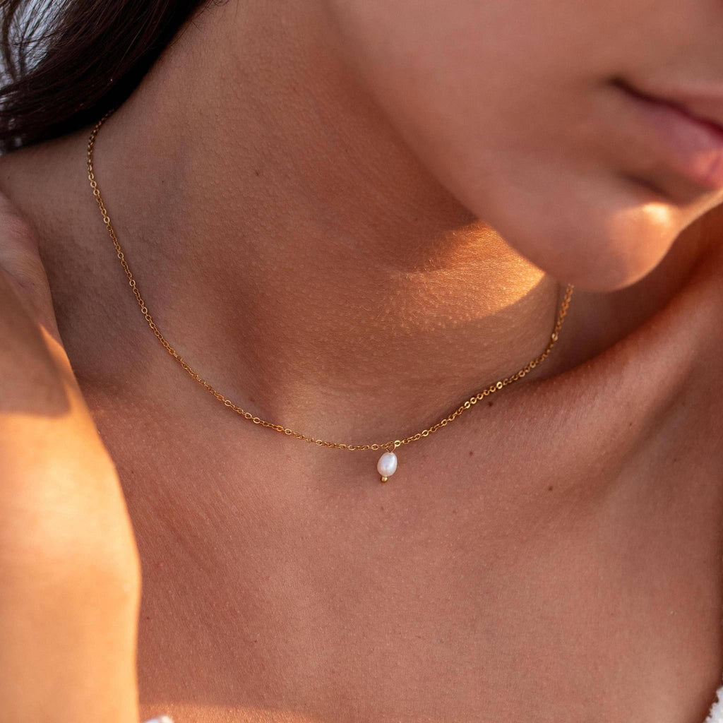 Gold necklace with a pearl pendant on a person's neck