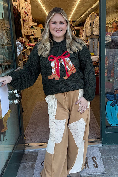 Woman wearing a sweater with a red bow design, standing in front of a store entrance.