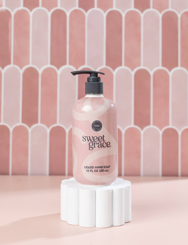 Sweet Grace liquid hand soap bottle on a white pedestal with a pink tiled background