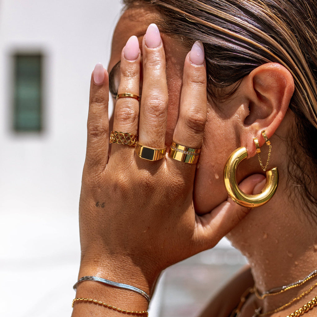 Close-up of a person wearing gold jewelry including rings and earrings.