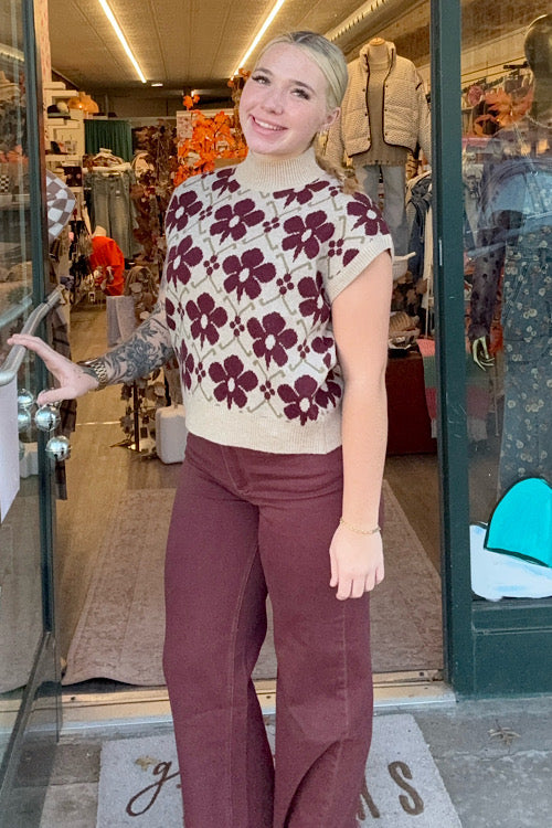 Woman wearing a floral sweater and burgundy pants standing in a store entrance.