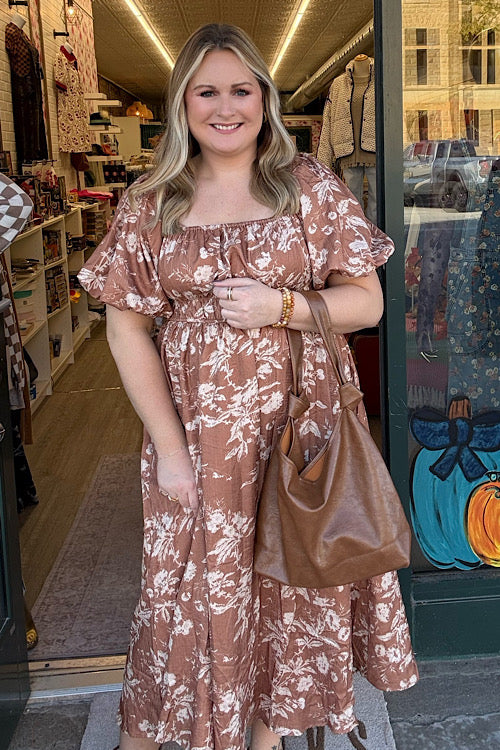 Woman in a floral dress holding a brown bag in front of a store entrance.