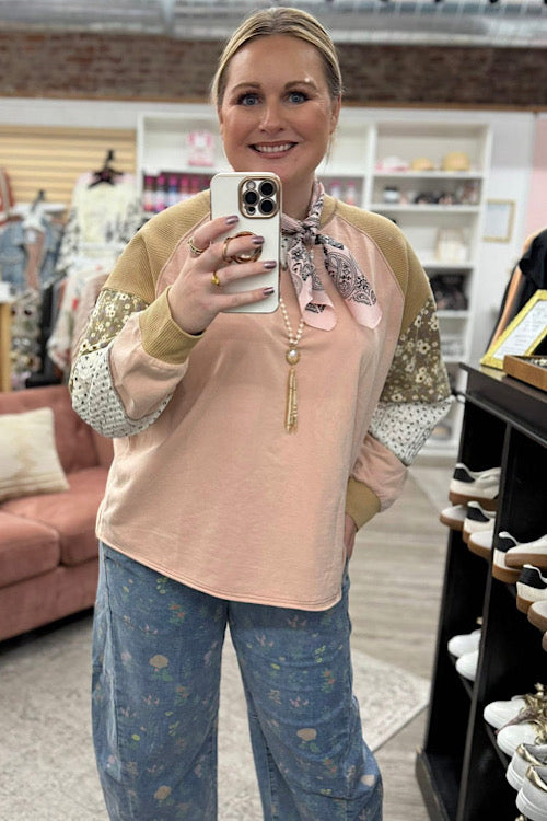 Woman taking a mirror selfie in a store wearing a beige sweater with floral patterns and blue pants.