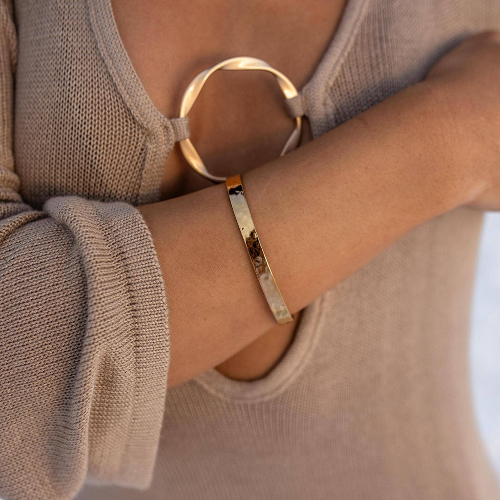 Gold bracelet on a wrist with a neutral background