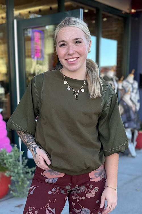 Woman wearing an olive green shirt and maroon pants with floral patterns, standing outdoors.