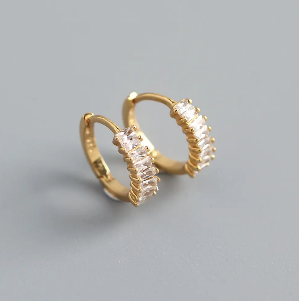 Gold hoop earrings with clear gemstones on a gray background