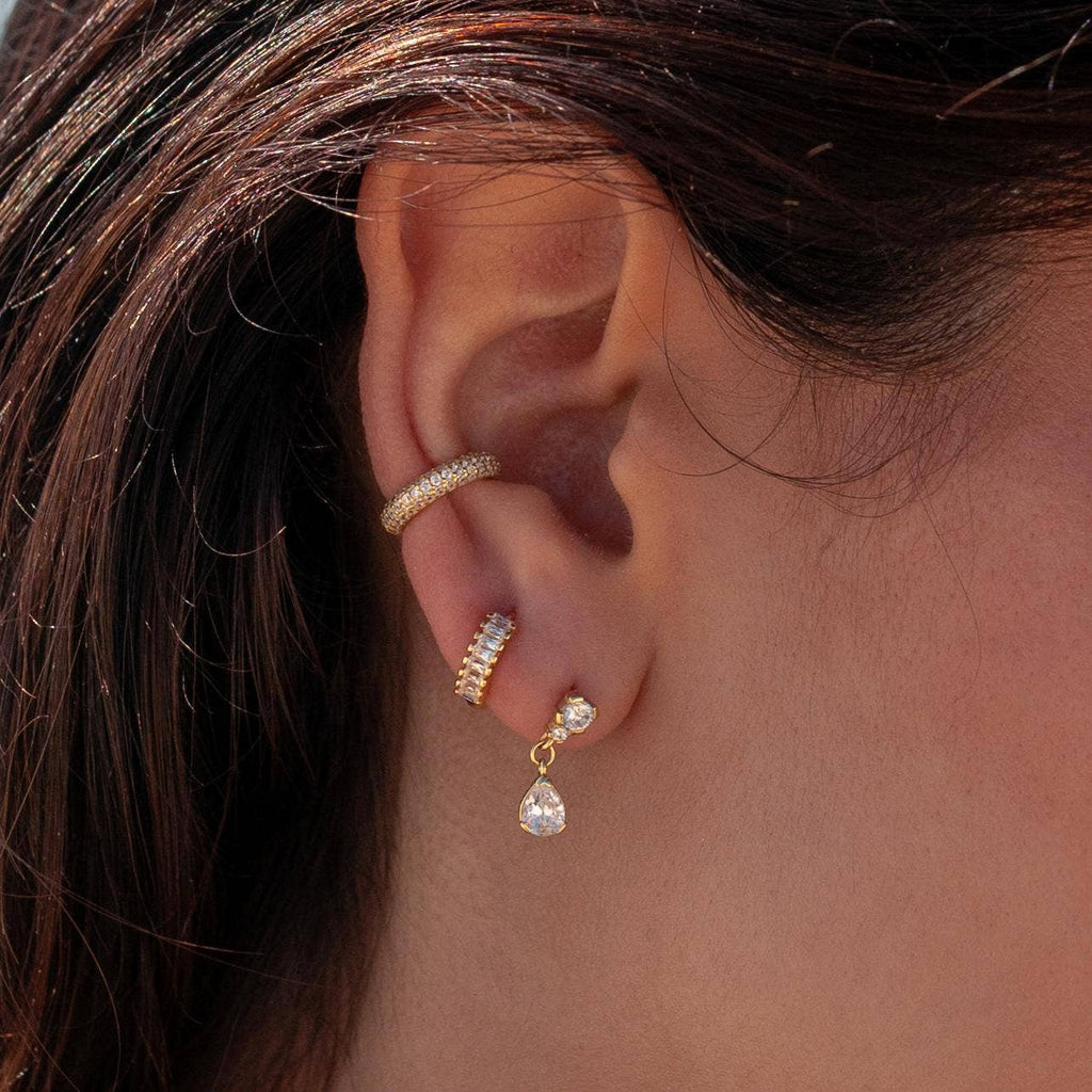Close-up of an ear wearing gold hoop and teardrop earrings with dark hair.