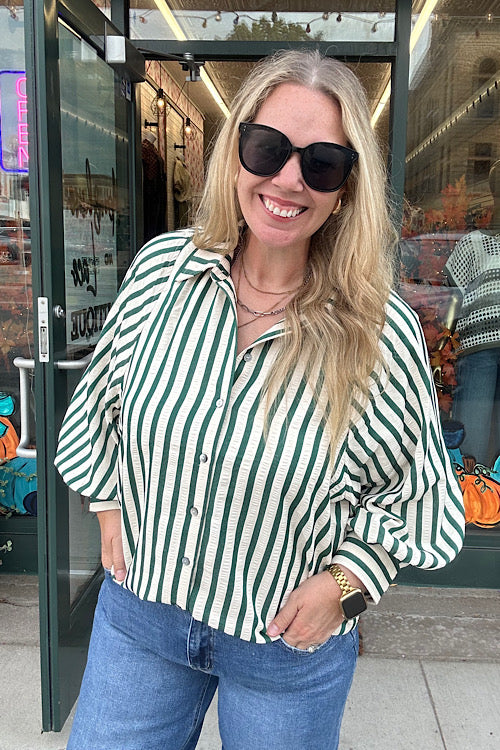 Woman wearing Eliza hunter green and cream vertical stripe button down top with relaxed fit and cuff detail, styled with denim jeans.